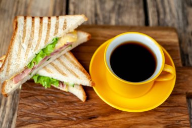 Jambon ve peynir ile taze ızgara sandviç ahşap doğrama tahtası üzerinde kahve fincan ile servis