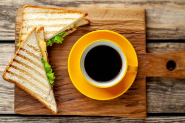 Jambon ve peynir ile taze ızgara sandviç ahşap doğrama tahtası üzerinde kahve fincan ile servis