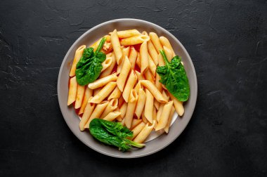 taş siyah arka plan üzerinde yeşil yaprakları ile servis domates soslu makarna