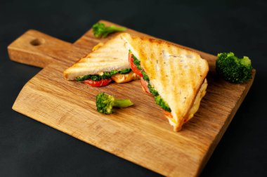 Ahşap doğrama tahtasında jambon, taze brokoli ve peynirile taze ızgara sandviçler