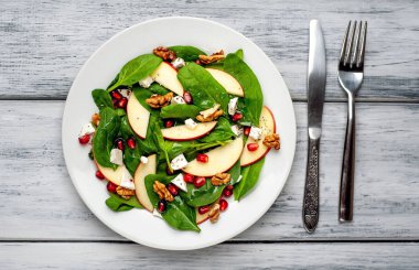 Ahşap arka plan üzerinde ıspanak yaprakları, peynir, nar tohumu, elma dilimleri ve fındık ile taze salata 