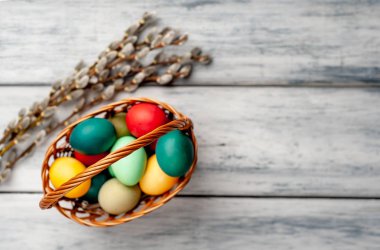 Beyaz ahşap arka planda renkli Paskalya yumurtaları ve kedi söğüt dalları ile sepet