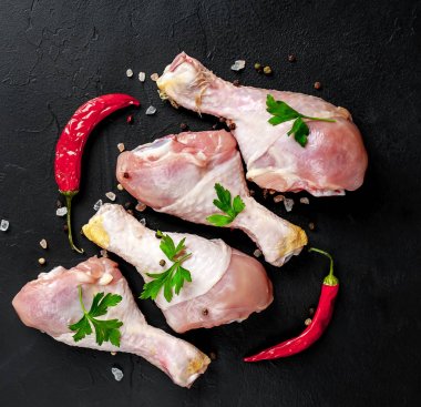 Baharat, biber ve maydanoz yaprakları ile tavuk bacakları siyah taş arka plan üzerinde