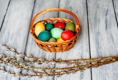 Beyaz ahşap arka planda renkli Paskalya yumurtaları ve kedi söğüt dalları ile sepet