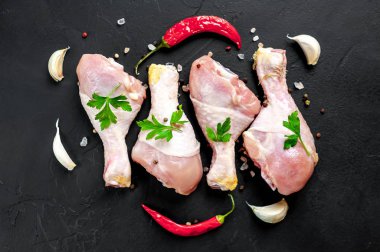 Baharat, biber ve maydanoz yaprakları ile tavuk bacakları siyah taş arka plan üzerinde