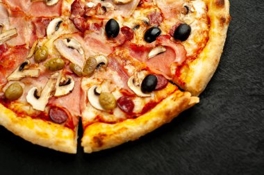Siyah taş arka plan üzerinde mantar, domates, zeytin ve jambon ile taze ev yapımı pizza