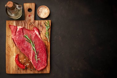 Taş arka planda baharat ve biberiye ile çiğ sığır eti biftek