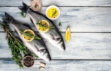 Gri ahşap arka plan üzerinde limon dilimleri ve biberiye dalları ile çiğ balık