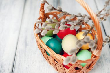 Beyaz ahşap arka planda renkli Paskalya yumurtaları ve kedi söğüt dalları ile sepet