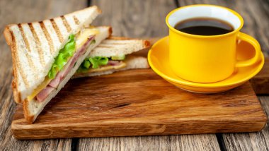 Jambon ve peynir ile taze ızgara sandviç ahşap doğrama tahtası üzerinde kahve fincan ile servis