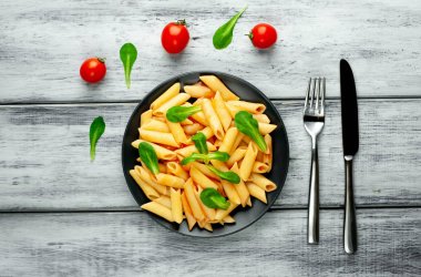 Ahşap arka plan üzerinde domates sosu ve yeşil yaprakları ile Makarna 