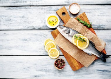 Ahşap doğrama tahtası üzerinde limon dilimleri ve biberiye dalları ile çiğ balık