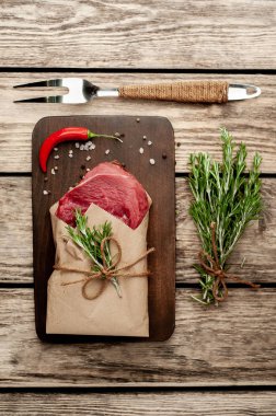 Ahşap doğrama tahtası üzerinde biberiye dalları ile zanaat kağıt sarılmış çiğ sığır eti biftek