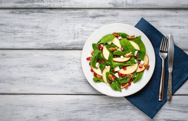 Ahşap arka plan üzerinde ıspanak yaprakları, peynir, nar tohumu, elma dilimleri ve fındık ile taze salata 