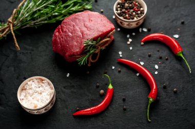 Siyah taş arka plan üzerinde yeşil biberiye dalları ve baharatlar ile Çiğ biftek 