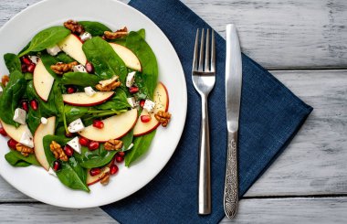 Ahşap arka plan üzerinde ıspanak yaprakları, peynir, nar tohumu, elma dilimleri ve fındık ile taze salata 