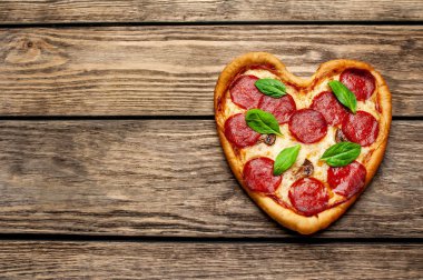 ahşap arka plan üzerinde salam ve taze fesleğen yaprakları ile peynir kalp pizza