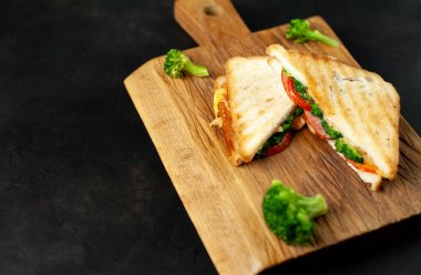 Ahşap doğrama tahtasında jambon, taze brokoli ve peynirile taze ızgara sandviçler