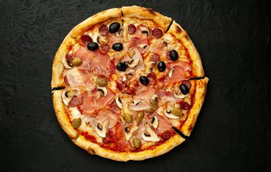 Siyah taş arka plan üzerinde mantar, domates, zeytin ve jambon ile taze ev yapımı pizza