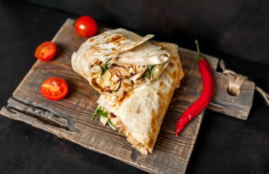 Geleneksel Meksika burrito tavuk ve sebze ile sarılmış ahşap doğrama tahtası üzerinde olgun domates ile servis 