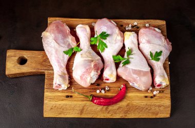 Ahşap doğrama tahtası üzerinde baharat, biber ve maydanoz yaprakları ile Tavuk bacakları 