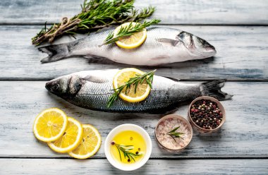 Gri ahşap arka plan üzerinde limon dilimleri ve biberiye dalları ile çiğ balık