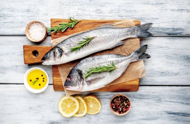 Ahşap doğrama tahtası üzerinde limon dilimleri ve biberiye dalları ile çiğ balık