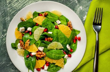 Ispanak yaprakları, peynir, nar tohumu, portakal dilimleri ve taş arka plan üzerinde fındık ile taze salata 