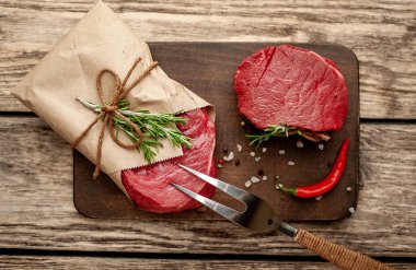 Ahşap arka plan üzerinde zanaat kağıt sarılmış baharat ile Çiğ biftek 