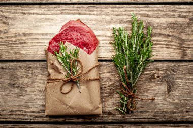 Ahşap arka plan üzerinde biberiye dalları ile zanaat kağıt sarılmış çiğ sığır eti biftek 