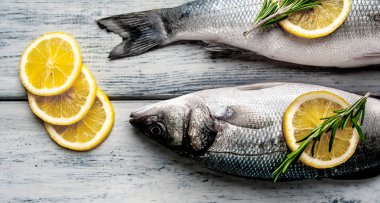 Gri ahşap arka plan üzerinde limon dilimleri ve biberiye dalları ile çiğ balık