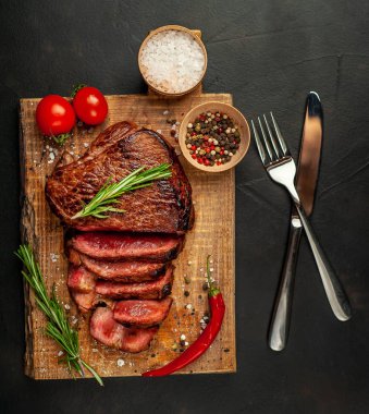 Taze sığır eti biftek ahşap tahta üzerinde domates, biberiye biberiye ve biberiye dalları ile servis