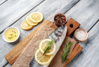 Ahşap doğrama tahtası üzerinde limon dilimleri ve biberiye dalları ile çiğ balık