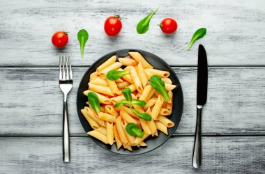 Ahşap arka plan üzerinde domates sosu ve yeşil yaprakları ile Makarna 