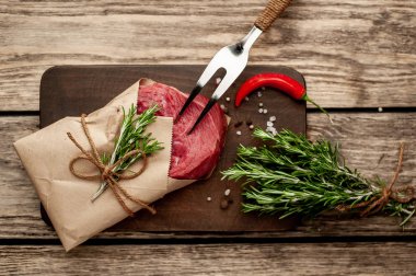 Ahşap doğrama tahtası üzerinde biberiye dalları ile zanaat kağıt sarılmış çiğ sığır eti biftek