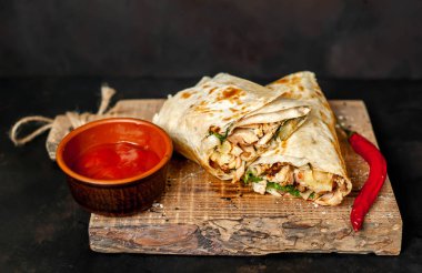 Ahşap doğrama tahtası üzerinde baharatlı sos ile tavuk ve sebze ile sarılmış geleneksel Meksika burrito 