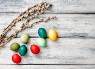 Beyaz ahşap arka planda renkli Paskalya yumurtaları ve kedi söğüt dalları yığını