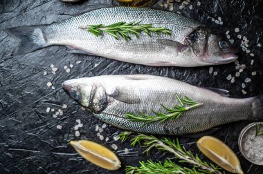 Siyah taş arka plan üzerinde limon, baharat ve biberiye dalları ile çiğ balık