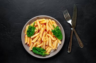 taş siyah arka plan üzerinde yeşil yaprakları ile servis domates soslu makarna