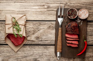 Dilimlenmiş biftek ve çiğ biftek ahşap arka plan üzerinde zanaat kağıt sarılmış