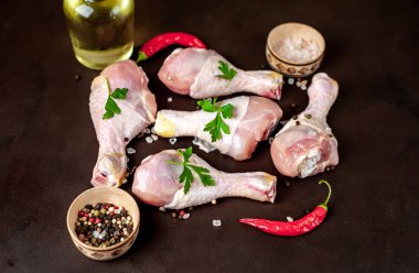 Siyah taş arka plan üzerinde baharat, tuz, zeytinyağı ve maydanoz yaprakları ile tavuk bacakları