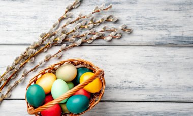 Beyaz ahşap arka planda renkli Paskalya yumurtaları ve kedi söğüt dalları ile sepet