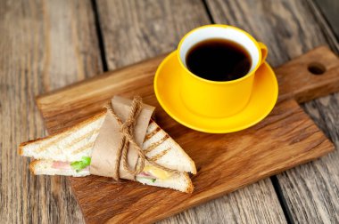 Jambon ve peynir ile taze ızgara sandviç ahşap doğrama tahtası üzerinde kahve fincan ile servis