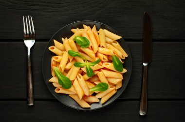 taş siyah arka plan üzerinde yeşil yaprakları ile servis domates soslu makarna