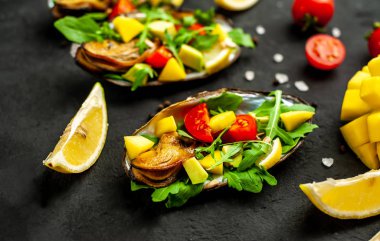 Siyah beton arka plan üzerinde avokado, arugula, mango, domates ve limon dilimleri ile pişmiş midye