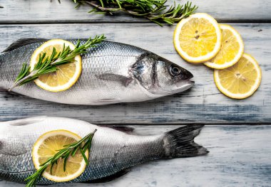 Gri ahşap arka plan üzerinde limon dilimleri ve biberiye dalları ile çiğ balık