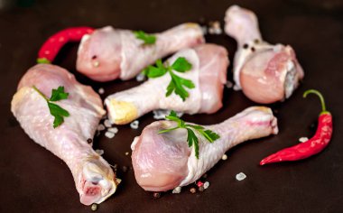 Baharat, biber ve maydanoz yaprakları ile tavuk bacakları siyah taş arka plan üzerinde