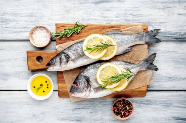 Ahşap doğrama tahtası üzerinde limon dilimleri ve biberiye dalları ile çiğ balık