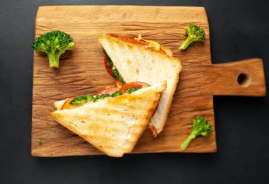 Ahşap doğrama tahtasında jambon, taze brokoli ve peynirile taze ızgara sandviçler