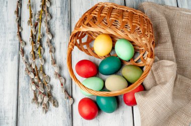 Beyaz ahşap arka planda renkli Paskalya yumurtaları ve kedi söğüt dalları ile sepet